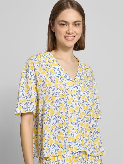 Frauenmodel trägt Relaxed Fit Hemdbluse aus reiner Viskose Modell 'BARRI' von Pieces mit floralem Allover-Muster in Gelb und Blau, Nahaufnahme Oberkörper.