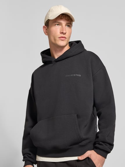 Männermodel trägt Relaxed Fit Hoodie aus Baumwoll-Mix mit Label-Detail von PROHIBITED in Schwarz, große Känguru-Tasche, Nahaufnahme Oberkörper.