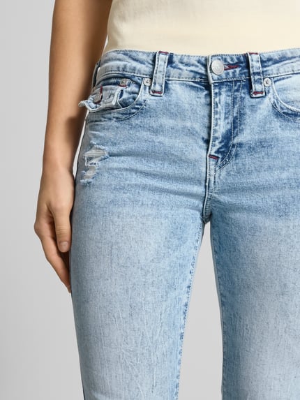 Frauenmodel trägt Flared Jeans im Destroyed-Look Modell 'BECCA' von TRUE RELIGION aus Baumwoll-Elasthan-Mix, Nahaufnahme Hüfte. Bundweite 40 cm, Innenbeinlänge 83 cm bei Größe 27, helle Blautöne, sichtbare Textur.