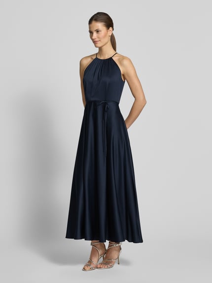 Frauenmodel trägt Cocktailkleid aus Satin mit Bindegürtel von Jake*s Cocktail in Dunkelblau, A-Linie, Neckholder, Ganzkörperansicht von vorne.