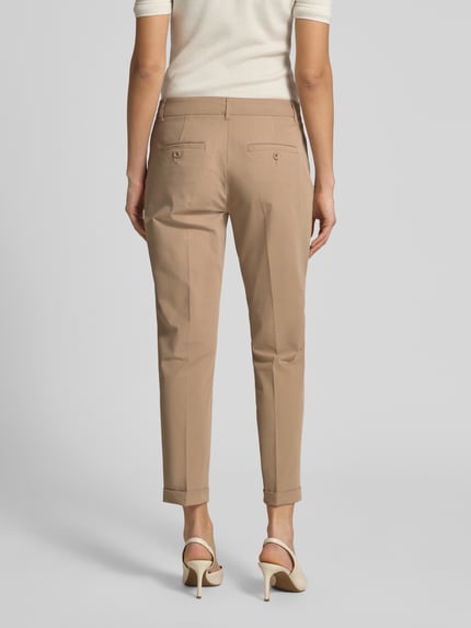 Vrouwenmodel draagt chino uit Techno Cotton Superstretch model 'UTE' van Raffaello Rossi in beige, straight fit, verkorte pasvorm, met steek- en achterzakken, persplooien, vaste omslag aan de pijpen, riemlussen, knoop- en ritssluiting, elastische materiaalmix met katoen, model vanuit volledige achteraanzicht.
