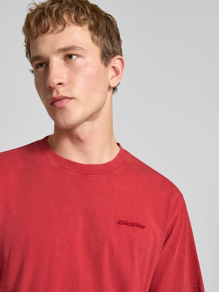 Männermodel trägt T-Shirt mit Rundhalsausschnitt und Label-Stitching von Dickies in Rot, reine Baumwolle, Regular Fit, Nahaufnahme Oberkörper.