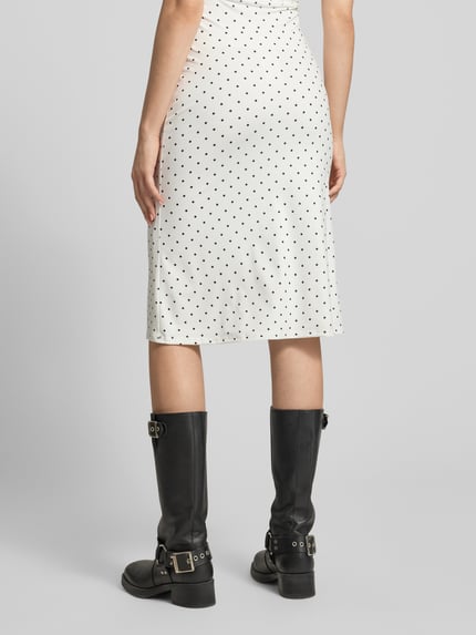 Frauenmodel trägt Midirock im Allover-Look Modell '90s von Gina Tricot aus Material-Mix mit Stretch-Anteil in Weiß mit schwarzen Punkten, figurbetonter Schnitt, Damen, Bundweite 36 cm, Gesamtlänge 62 cm, Ganzkörperansicht Rückansicht.
