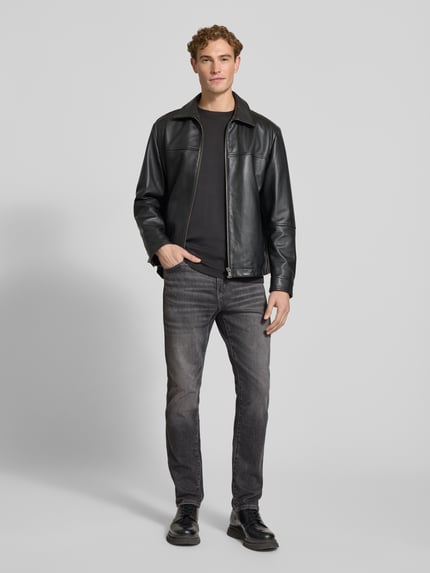 Męski model nosi szare jeansy o kroju tapered fit z bawełnianego mixu Tapered Fit Jeans aus Baumwoll-Mix Modell 'Redford' od Wrangler, widok całej sylwetki z przodu.