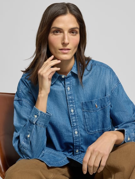 Frauenmodel trägt Oversized Hemdbluse in Denim-Optik von Polo Ralph Lauren, reine Baumwolle, Hemdblusenkragen, Knopfleiste, Brusttasche, Label-Stitching, Nahaufnahme Oberkörper.