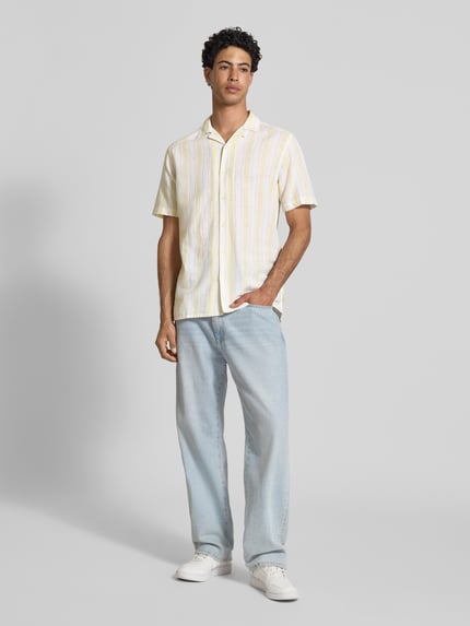 Männermodel trägt Regular Fit Leinenhemd aus Baumwoll-Leinen-Mix Modell 'CAIDEN' von Only & Sons mit gelb-weißen Streifenmuster, Kurzarm, Resortkragen, durchgehender Knopfleiste; Ganzkörperansicht von vorne.