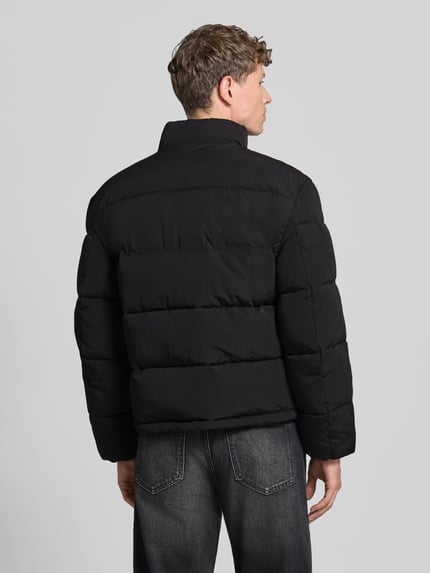 Männermodel trägt schwarze Daunenjacke mit Logo-Patch von HUGO, Stehkragen, Reißverschluss, Taschen, uni, Nähte, Ganzkörperansicht Rückansicht