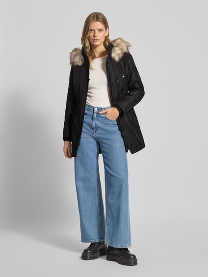 Vrouwenmodel draagt zwarte Shaped Fit Parka met Label Patch model 'IRIS' van Only, met capuchon, lange mouwen, zij- en borstzakken, effen look, regular fit, knopen, ritssluiting, storm cuffs; vooraanzicht hele lichaam.