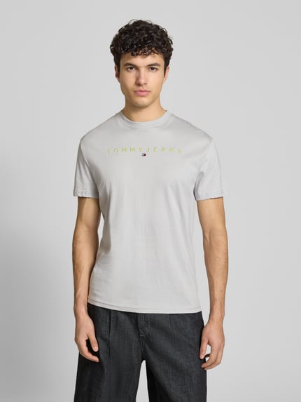 Männermodel trägt Regular Fit T-Shirt aus reiner Baumwolle von Tommy Jeans in Unifarbe mit Label Stitching, Jerseystruktur, Ganzkörperansicht von vorne.