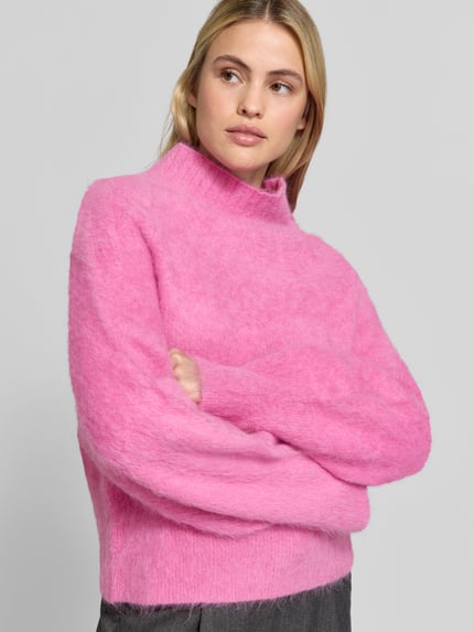 Frauenmodel trägt Sweatshirt mit Mock Neck Modell 'PROMISY' von IRO in knalligem Pink, Strukturmuster, gerippte Abschlüsse, Nahaufnahme Oberkörper.