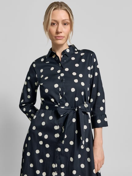 Frauenmodel trägt Regular Fit Blusenkleid aus Baumwoll-Mix von s.Oliver BLACK LABEL in Optik:Allover-Muster mit Polka-Dots, Knopfleiste, Taillengürtel, Langarm mit Manschette, Hemdblusenkragen, seitliche Eingrifftaschen, Farbe dunkelblau mit weißen Punkten, Struktur glatt, Midi-Länge, Ganzkörperansicht von vorne.