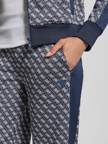 Frauenmodel trägt Wide Leg Sweatpants im Allover-Look Modell 'MAYA' von Guess Activewear mit elastischem Bund und gemustertem Stoff, Nahaufnahme Oberkörper.