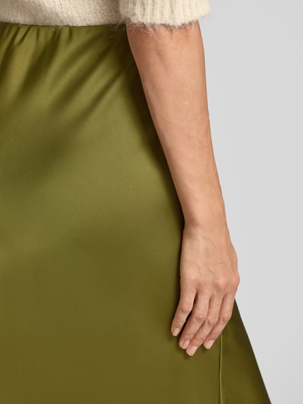 Frauenmodel trägt Midi-Rock aus Satin Modell 'Ve44rona' von ZABAIONE, olivgrün, glatte Textur, Detailaufnahme Nahaufnahme Oberkörper. Damen Midi-Rock von ZABAIONE, Satin, A-Linie, elastischer Bund, Bundweite bei Größe S: 35 cm, Gesamtlänge 95 cm.