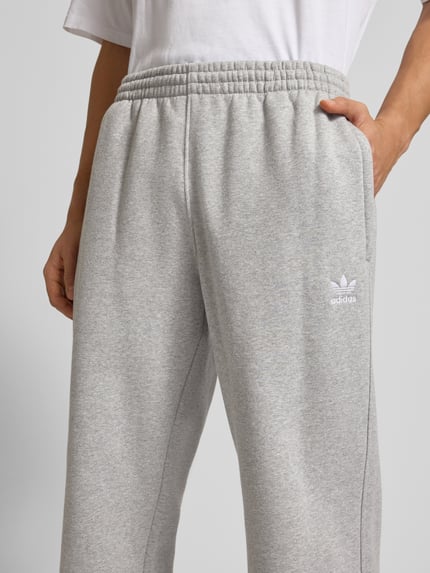 Männermodel draagt Sweathose met Labelstitching en elastische band van adidas Originals, katoenmix, wijd been, binnenbeenlengte maat M 40 cm, detailopname.