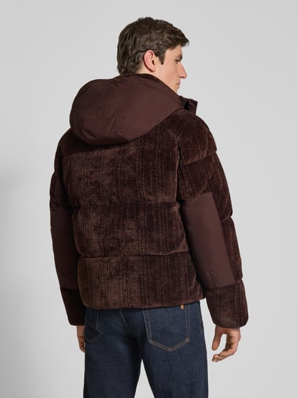 Männermodel trägt Pufferjacke mit abnehmbarer Kapuze von BOSS Orange aus Cord in Dunkelbraun mit Stehkragen, Struktur und Reißverschlusstaschen, Ganzkörperansicht Rückansicht.