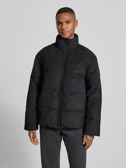 Mannenmodel draagt Regular Fit gewatteerd jack uit corduroy van Tom Tailor Denim, effen zwart, ritssluiting, steekzakken, lange mouw, opstaande kraag, labelstitching, geribde rompzoom, vooraanzicht, Ganzkörperansicht von vorne.