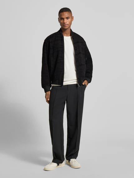 Männermodel trägt Bomberjacke mit Reißverschluss von Armani Exchange, schwarzer Material-Mix mit Stretch-Anteil, Regular-Fit, gerippte Abschlüsse, Stehkragen, Reißverschluss, Eingrifftaschen, glatte und strukturierte Texturen, Ganzkörperansicht von vorne.