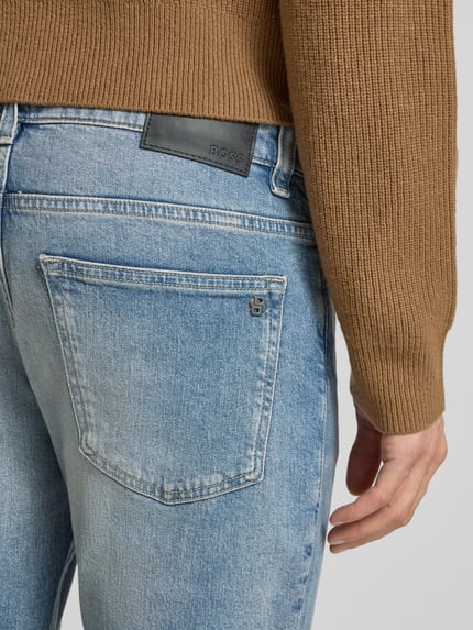 Mężczyzna nosi Slim Fit Jeans aus Baumwoll-Mix Modell 'DELAWARE BO' od BOSS Orange, jasnoniebieski denim, detal z tyłu, zbliżenie na kieszeń.