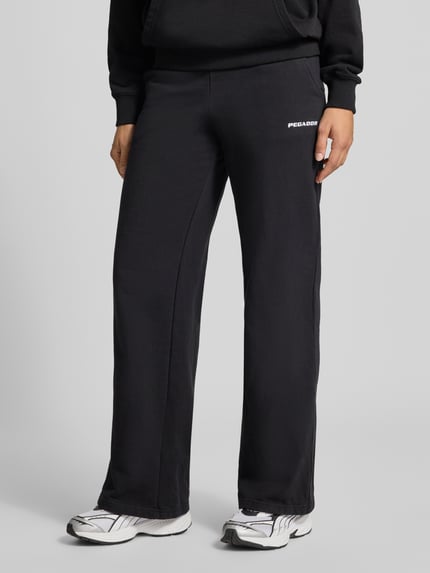 Frauenmodel trägt Wide Fit Sweatpants aus Baumwoll-Mix Modell 'ANNI' von PEGADOR in Schwarz mit Label-Detail, Nahaufnahme Unterkörper.
