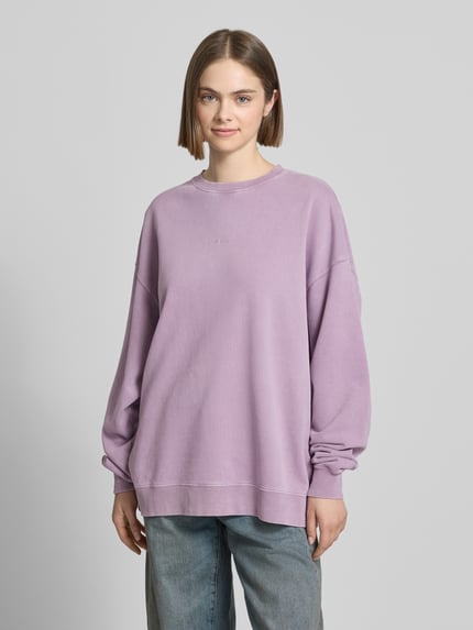 Vrouwenmodel draagt oversized dames sweatshirt van puur katoen, model 'Farmers Market' van OH APRIL, lavendel, logostitching, statementprint op de rug, ronde hals, verlaagde schouders, oversized fit, voorkant volledig zichtbaar, ganzkörperansicht van voren.