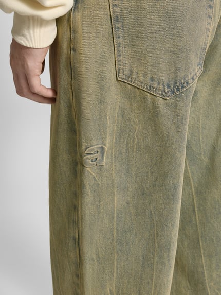 Mężczyzna nosi Wide Fit Jeans mit Viskose-Anteil Modell 'Everyday' od ANOTHER COTTON LAB, bawełniany miks, detal haftu, zbliżenie na nogawkę