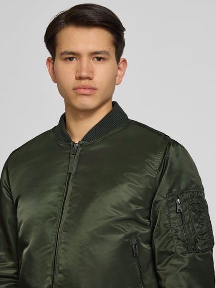 Männermodel trägt Bomberjacke mit Kapuze und Reißverschlusstaschen von Superdry in Grün, Regular-Fit, Nahaufnahme Oberkörper. Rückenlänge 56 cm, Schulterbreite 45 cm, Brustweite 60 cm, Ärmellänge 68 cm, Größe M.