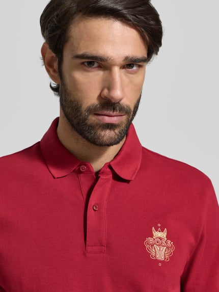 Männermodel trägt Regular Fit Poloshirt aus reiner Baumwolle Modell 'QIANG' von BOSS, Optik: Unifarben, Motiv-Label-Print, Nahaufnahme Oberkörper.