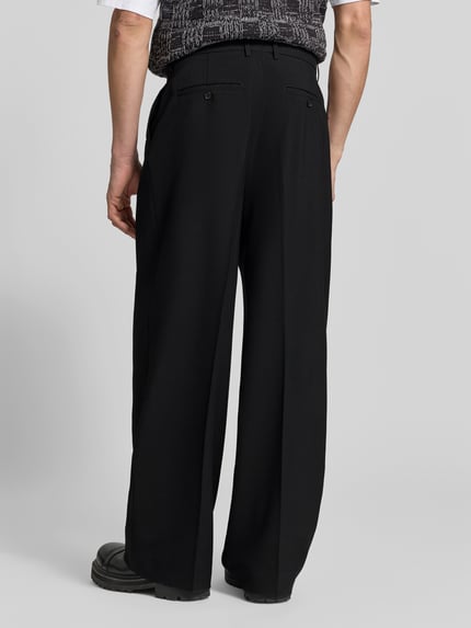 Männermodel trägt Relaxed Fit Stoffhose aus Woll-Mix von Filippa K in Schwarz mit Bundfalten und Gesäßtaschen, Ganzkörperansicht Rückansicht.