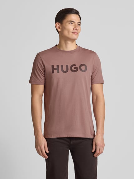 Męski model nosi Regular Fit T-Shirt aus reiner Baumwolle Modell 'DULIVIO' von HUGO, kolor jednolity, nadruk logo, widok całej sylwetki z przodu.