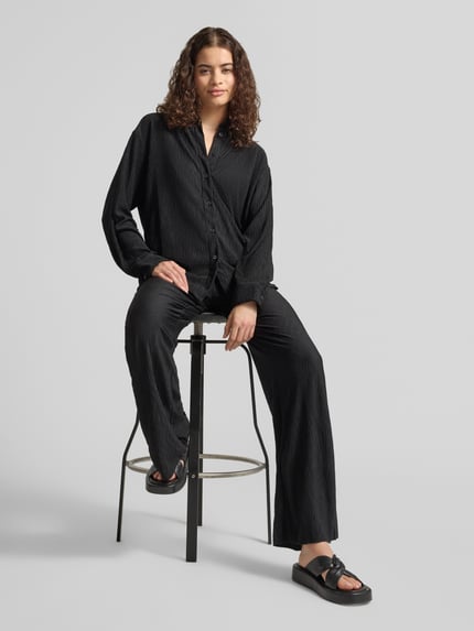 Frauenmodel trägt schwarze Flared Cut Hose mit Plisseefalten und elastischem Bund von REVIEW, Material-Mix mit Stretch-Anteil, Ganzkörperansicht von vorne.