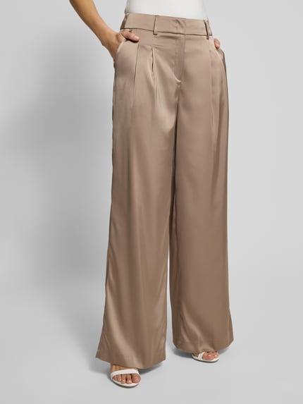 Modelka kobieca nosi Stoffhose mit Gesäßtaschen von Christian Berg Woman Selection, beżowy kolor, szeroki krój, tkanina z domieszką stretchu, zbliżenie na dolną część ciała.