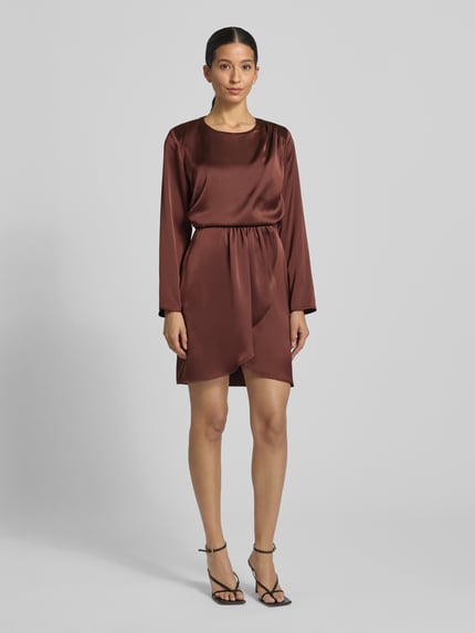 Frauenmodel trägt knielanges Cocktailkleid mit Rundhalsausschnitt von Rinascimento aus Satin in Braun, körpernahe Passform, asymmetrischer Saum, Rückenlänge 91 cm, Brustweite 47 cm, Ärmellänge 59 cm, Ganzkörperansicht von vorne.
