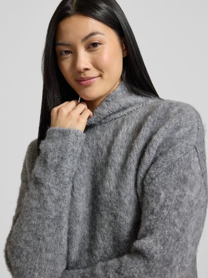 Frauenmodel trägt Strickpullover mit Stehkragen und überschnittenen Schultern von Milano Italy in Grau, flauschige Textur, Nahaufnahme Oberkörper. Material-Mix mit Mohair-Anteil, Regular Fit.