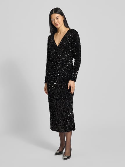 Frauenmodel trägt schwarzes Midikleid mit V-Ausschnitt, Pailletten, tailliertem Schnitt und Wickel-Optik, Modell 'FAITH' von Vila, Ganzkörperansicht von vorne