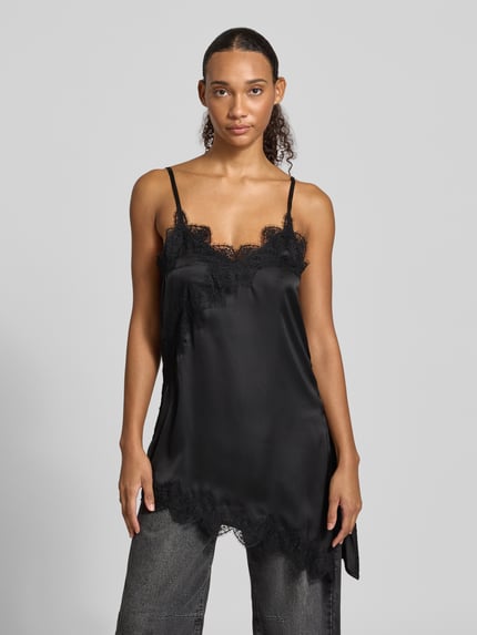 Modelka kobieca nosi A-Linie Freizeitkleid mit Spitzenbesatz Modell 'ELVA' von PIECES w czarnym kolorze, jednolita optyka, aplikacja z koronki, cienkie ramiączka, asymetryczne wykończenie dołu, widok całej sylwetki z przodu.