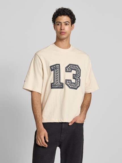 Męski model trägt T-Shirt mit Ketten-Stickerei und Rundhalsausschnitt von REVIEW, bawełna, krój relaxed fit, długość tyłu w rozmiarze M: 65 cm, jasny kolor, przód zdobi ciemny haft, gładka faktura, Ganzkörperansicht von vorne.