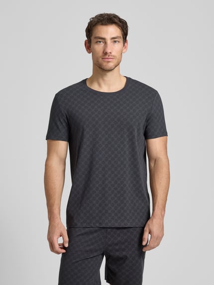 Męski model nosi T-Shirt mit Logo-Muster und Rundhalsausschnitt od JOOP! Collection, bawełna z domieszką elastanu, krój regular fit, ciemnoszary, krótki rękaw, długość tyłu w rozmiarze M: 68 cm, widok całej sylwetki z przodu.