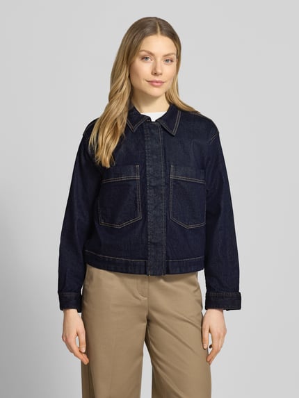 Frauenmodel trägt Regular Fit Jeansjacke aus Baumwoll-Mix von Tom Tailor mit Denim-Optik, Umlegekragen, Druckknopfleiste, Brusttaschen, Twill-Materialverarbeitung, Motiv-Stitching und Rückenpasse, Ganzkörperansicht von vorne.