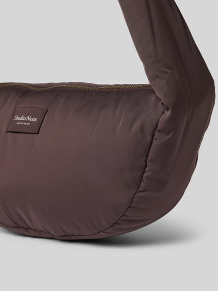 Produktfoto, braune Crossbody Bag aus Teddyfell mit Logo-Detail von Studio Noos, Reißverschluss, verstellbarer Schulterriemen, Breite 40 cm, Länge 22 cm, Tiefe 11 cm, Schulterriemen 64 cm
