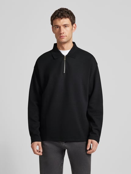 Männermodel trägt Sweatshirt mit Polokragen und Reißverschluss von CK Calvin Klein, Strukturmuster, Relaxed-Fit, Material-Mix, Ganzkörperansicht von vorne.
