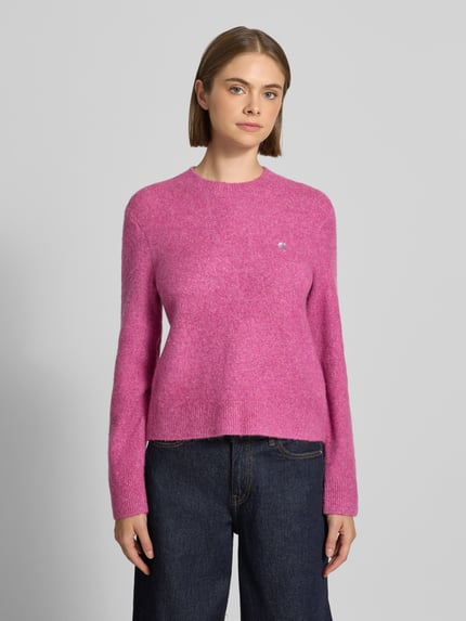 Frauenmodel trägt Strickpullover mit Label-Detail Modell 'Curtis' von Carhartt Work In Progress in Pink, feine Textur, taillierte Passform, Ganzkörperansicht von vorne.