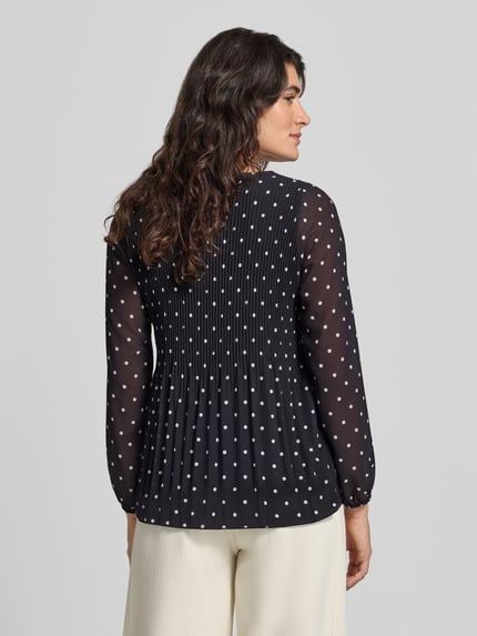 Männermodel trägt bluzka o kroju loose fit z plisami, okrągły dekolt, elastyczne zakończenia rękawów, Model 'Ka44na' od ZABAIONE, długość tyłu w rozmiarze S: 61 cm, długość rękawów w rozmiarze S: 54 cm, czarny z białymi kropkami, struktura plisów, faktura lekko transparentna, tył, Ganzkörperansicht Rückansicht.