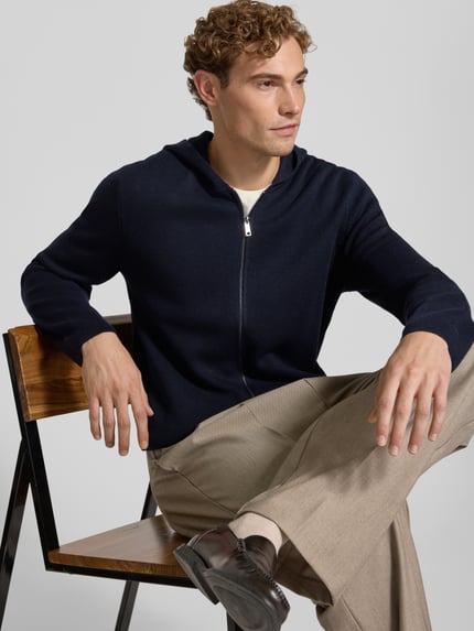 Männermodel trägt Regular Fit Strickjacke mit Lanawoll-Anteil von Christian Berg Men in Dunkelblau, Zipper und Kapuze, Nahaufnahme Oberkörper, Material-Mix.