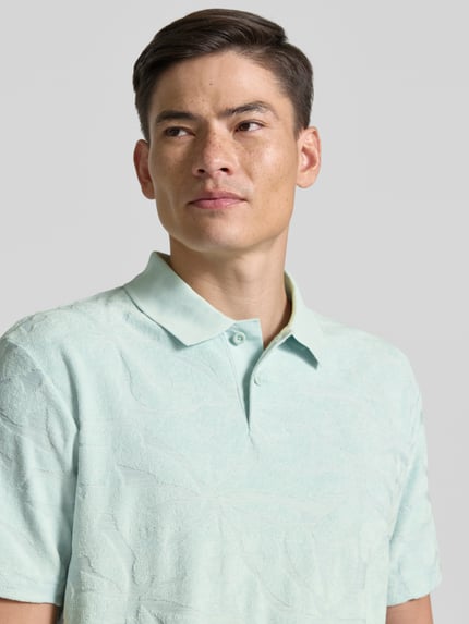 Männermodel trägt Regular Fit Poloshirt aus Baumwoll-Mix Modell 'PE_FLOWER' von BOSS Orange in Hellgrün mit Struktur, Nahaufnahme Oberkörper.