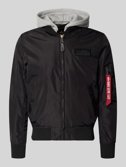Produktfoto, schwarzer Blouson mit grau melierter Sweat-Kapuze, Armtasche mit rotem Logo-Anhänger, Alpha Industries Blouson mit Logo-Anhänger Modell 'MA-1 TT', lockere Passform, elastische Abschlüsse, Label-Patch, Reißverschluss, glatte Textur