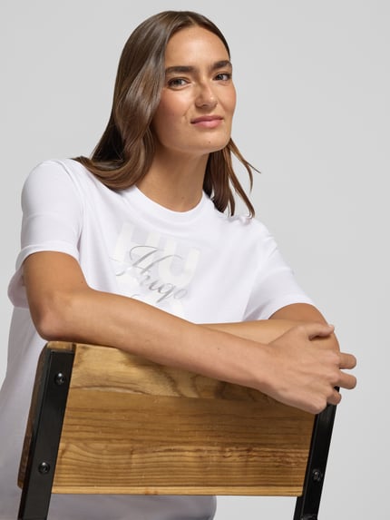 Kobiece model prezentuje damski t-shirt Regular Fit T-Shirt aus reiner Baumwolle Modell 'Dashire_5' od HUGO, biały, gładki materiał, z przodu nadruk, półzbliżenie górnej części ciała, damski t-shirt od HUGO.