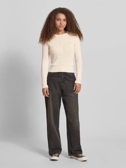 Frauenmodel trägt Strickpullover mit Zopfmuster und Label-Stitching von REVIEW, cremefarben, Baumwoll-Mix, Regular-Fit, Rundhalsausschnitt, Ganzkörperansicht von vorne.
