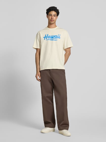 Männermodel trägt Relaxed Fit T-Shirt aus reiner Baumwolle Modell 'RICO' von Only & Sons, unifarbenes Jersey mit Motiv-Print, Ganzkörperansicht von vorne.