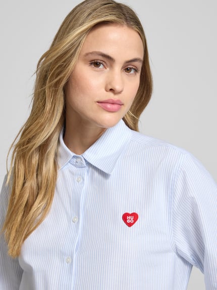 Kobiece modelka nosi Oversized Hemdbluse aus reiner Baumwolle Modell 'ERSELIA' od HUGO, białe niebieskie paski, detal z przodu, półzbliżenie górnej części ciała.