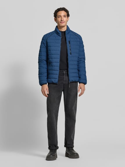 Männermodel trägt blaue Steppjacke mit Stehkragen und Reißverschlusstaschen von LERROS, Regular Fit, schwarze Hose, Ganzkörperansicht von vorne.